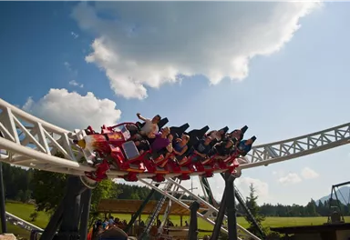 A roller coaster with people experiencing joy and excitement. The sky is clear and the sun is shining.