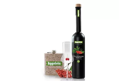 Eine Flasche Likör mit roten Beeren, ein Glas und eine dekorative Box. Das Produkt stammt von der Marke Aggstein.
