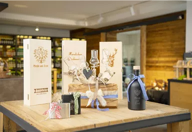 Ein dekorativer Tisch mit unterschiedlichen Geschenkpackungen und einem Flasche. Die Verpackungen sind aus Holz und enthalten schöne Designs.