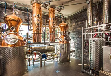 Eine moderne Brennerei mit glänzenden Kupferanlagen und Edelstahltanks. Die Wände sind mit Stein verkleidet und es gibt viel natürliches Licht.
