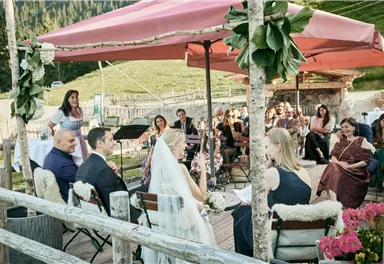 A romantic outdoor wedding ceremony under a pavilion. Surrounded by guests who are captivated listening to the bride and groom.