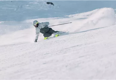 A skier glides gracefully over a snow-covered slope. The movement creates a spray of snow in the background.