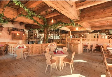 Ein gemütliches Restaurant mit Holzinterieur und warmem Licht. Die Tische sind hübsch gedeckt und es gibt grüne Pflanzen an den Wänden.
