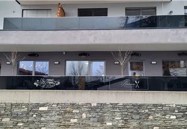Ein modernes Gebäude mit einem überdachten Balkon. Die Fassade ist schlicht und elegant, mit großen Fenstern und einer Steinmauer darunter.