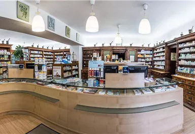 Eine helle Apotheke mit vielen Regalen voller Medikamente und einem modernen Empfangstresen. Die Wände sind dekoriert und die Atmosphäre wirkt einladend.