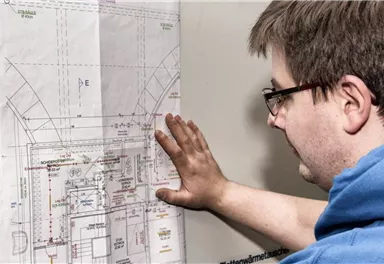 A man is looking at a construction plan on the wall. He has his hand on the plan and seems to be studying it closely.