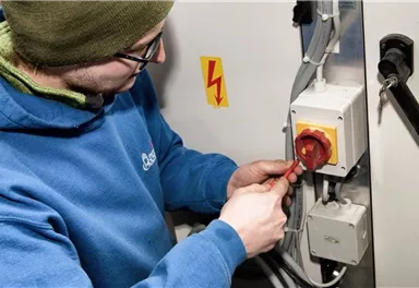 A technician is working on an electrical control box. He is using a tool to make a connection.