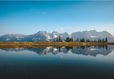 A picturesque mountain landscape with snow-covered peaks and a calm water that mirrors the clouds. The scenery is peaceful and inviting.