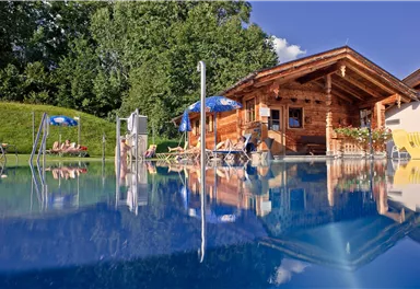 A beautiful wooden house next to a sparkling pool. Surrounded by green trees and loungers, the environment invites relaxation.