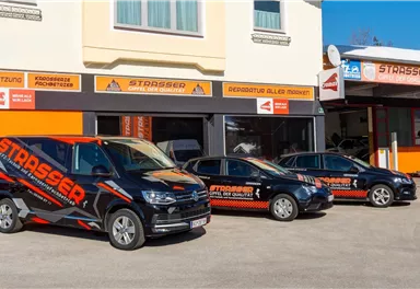 Three vehicles with eye-catching advertisements are parked in front of a store with an orange and white sign. The store offers services and has large windows.