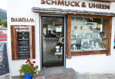A jewelry and watch store with an inviting storefront. Blooming plants stand outside the entrance door.