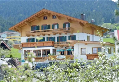A beautiful wooden house with several balconies in a green environment. The landscape is adorned with trees and mountains in the background.