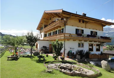 A charming two-story house with wooden ornaments and a large garden. The surroundings are green and sunny, perfect for outdoor relaxation.