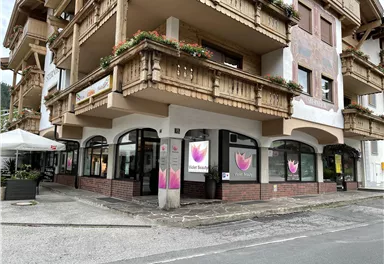 A modern building with a shop on the ground floor. The windows display colorful advertisements and there is an outdoor terrace.