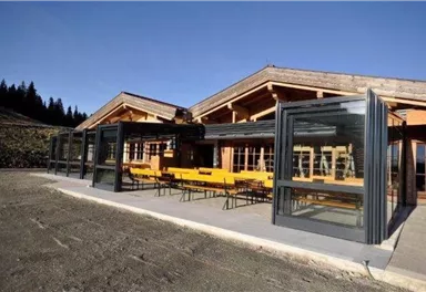 A modern building with large windows and a terrace. On the terrace, there are yellow tables and benches.