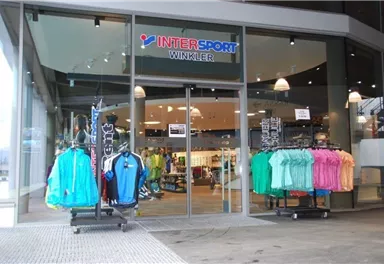 Ein Geschäftseingang mit dem Namen "INTER SPORT WINKLER". Vor der Tür stehen mehrere Kleiderständer mit bunter Sportbekleidung.
