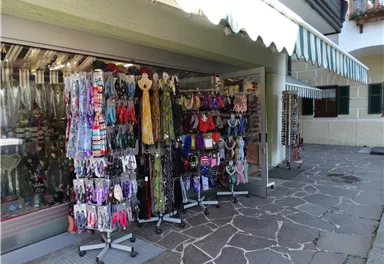 Ein Souvenirladen mit vielen bunten Schals und Schmuckstücken steht im Freien. Der Boden ist mit Steinplatten ausgelegt und es ist sonnig.