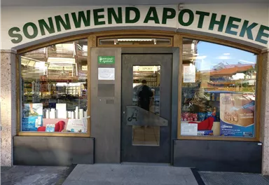 Eine Apotheke namens Sonnwend mit einem einladenden Eingang. Im Fenster sind verschiedene Produkte sichtbar.