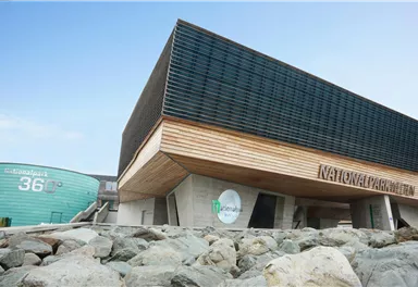 A modern building with wood and glass elements. It is located in a rocky environment and has a clear blue sky.