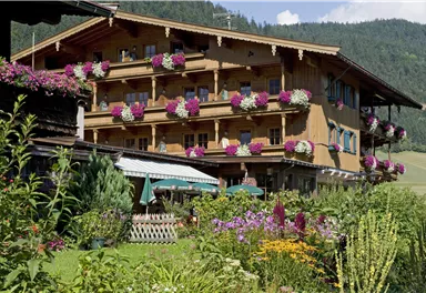Ein hübsches Holzhaus mit Balkonen, die mit bunten Blumen geschmückt sind. Im Vordergrund gibt es einen schönen Garten mit vielen Pflanzen und Blumen.