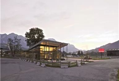 A modern building with a glass facade in a mountainous environment. The gentle evening ambiance and the surrounding mountains create an inviting atmosphere.