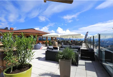 Eine moderne Dachterrasse mit Blick auf die Berge. Gemütliche Sitzgelegenheiten und Sonnenschirme laden zum Entspannen ein.