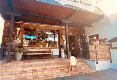An inviting farm shop with the sign "Wilder Käser" above the entrance. The entrance area is decorated with plants and has a cozy seating area.