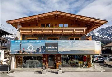 An old wooden building that houses a store for outdoor equipment. The shop displays large promotional banners and is located in a mountainous area.