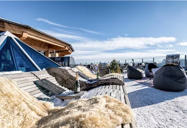 A cozy terrace in the mountains with loungers and bean bags. In the background, you can see a clear view of the sky and a snow-covered landscape.