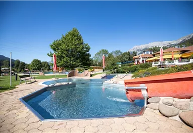 A beautiful pool area with smooth water and relaxing loungers. Surrounded by lush greenery and a clear blue sky.
