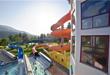 A water park with multiple slides and a swimming pool. The sun is shining, and the surroundings are green and inviting.