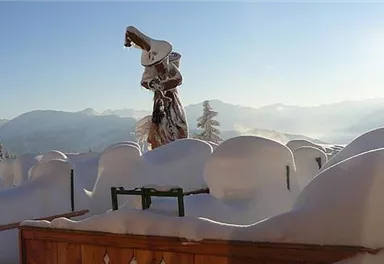 Eine verschneite Landschaft mit vielen schneebedeckten Hügeln. Im Vordergrund steht eine Statue, die von Schnee umgeben ist, während die Sonne scheint.