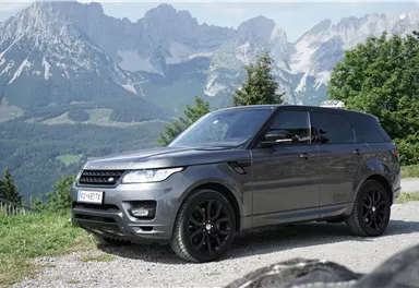 Ein eleganter SUV steht auf einem Schotterweg vor einer beeindruckenden Berglandschaft. Die malerischen Berge und der klare Himmel verleihen der Szene eine majestätische Atmosphäre.
