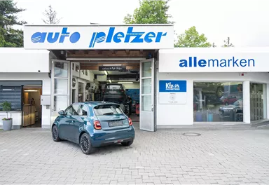 A workshop named "auto pletzer" with a modern car in the foreground. In the background, other vehicles and the inscription "all brands" are visible.