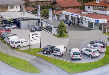 A car dealership with several vehicles on the premises. There is a modern building and a wide selection of cars.