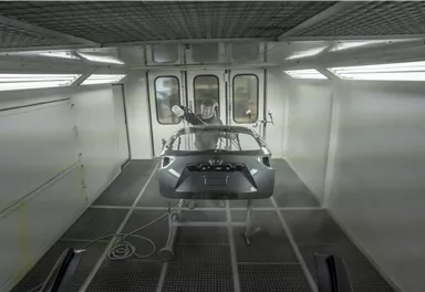 A painted car body stands in a modern paint booth. Bright lighting ensures optimal visibility during the painting process.