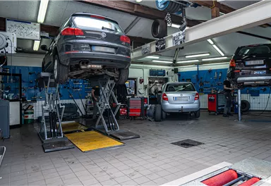 A car workshop with several cars on lifts. The walls are equipped with tools and equipment.