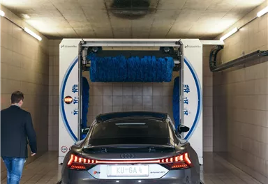 A car is being washed in a car wash. A person is walking towards the vehicle.