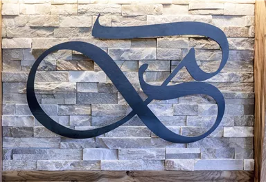 An artistic logo made of black metal, mounted on a textured stone wall. The curved lines of the logo give the design elegance and modernity.