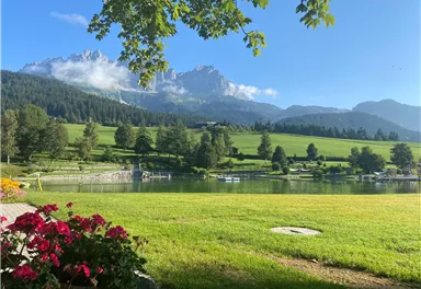 An idyllic landscape with a clear lake and green meadows. In the background, the majestic mountains rise into the sky.