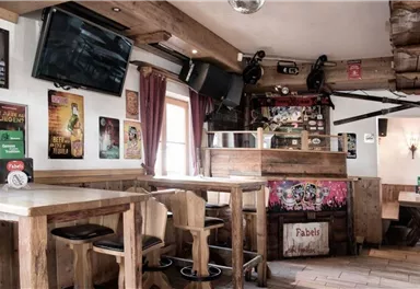 A cozy dining area with paneling and seating options. Various posters hang on the walls, and there are several screens.