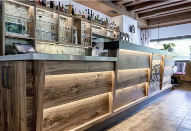 A modern bar with an elegant wooden counter and illuminated design. Behind the counter, shelves with various drinks are visible.
