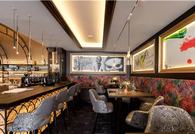 Ein modernes Restaurant mit stilvoller Einrichtung und einer langen Bar. Die Wände sind mit bunten Mustern und Kunstwerken dekoriert.