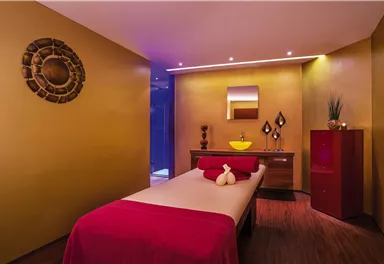 A stylish spa room with a massage bed and warm yellow tones. Decorative elements and soft lighting create a relaxing atmosphere.