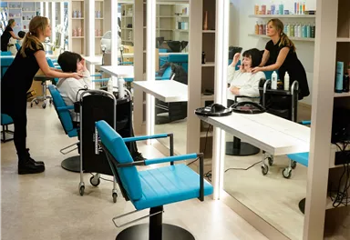 Ein moderner Friseursalon mit stilvollen blauen Stühlen. Eine Friseurin arbeitet an einem Kunden, während eine andere beim Styling hilft.
