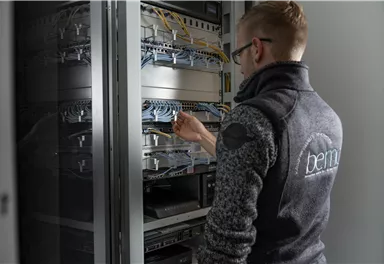 Ein Techniker arbeitet an einem Serverraum. Er verbindet Kabel in einem Netzwerk-Schrank.
