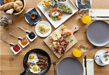 A hearty breakfast with a variety of dishes. This includes fresh rolls, eggs, cold cuts, and a selection of jams.
