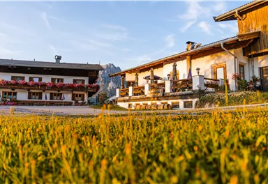 Ein charmantes Bauernhaus mit schöner Blumenbepflanzung liegt in einer malerischen Landschaft. Der sanfte Morgenlichtschein schafft eine einladende Atmosphäre.
