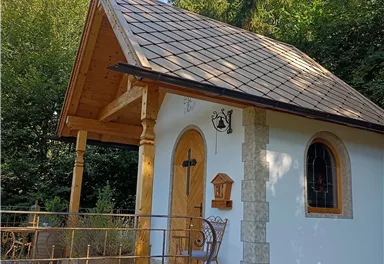 Ein kleines, charmantes Gebäude mit einem Holzschild und einem schrägen Dach. Es ist von Bäumen umgeben und hat einen gepflegten Garten.