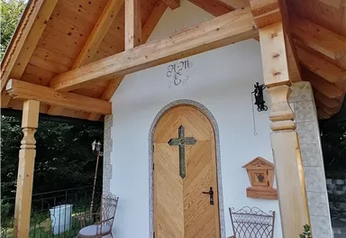 Ein charmantes kleines Haus mit einem Holzüberhang und einer schönen Eingangstür. Vor der Tür stehen zwei eiserne Stühle und dekorative Pflanzen.